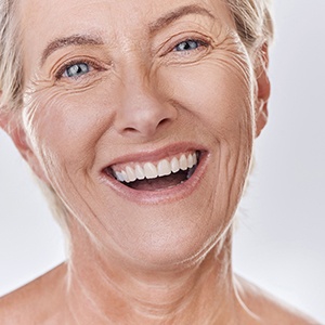 Facial close up of a woman with blue eyes smiling wearing dentures